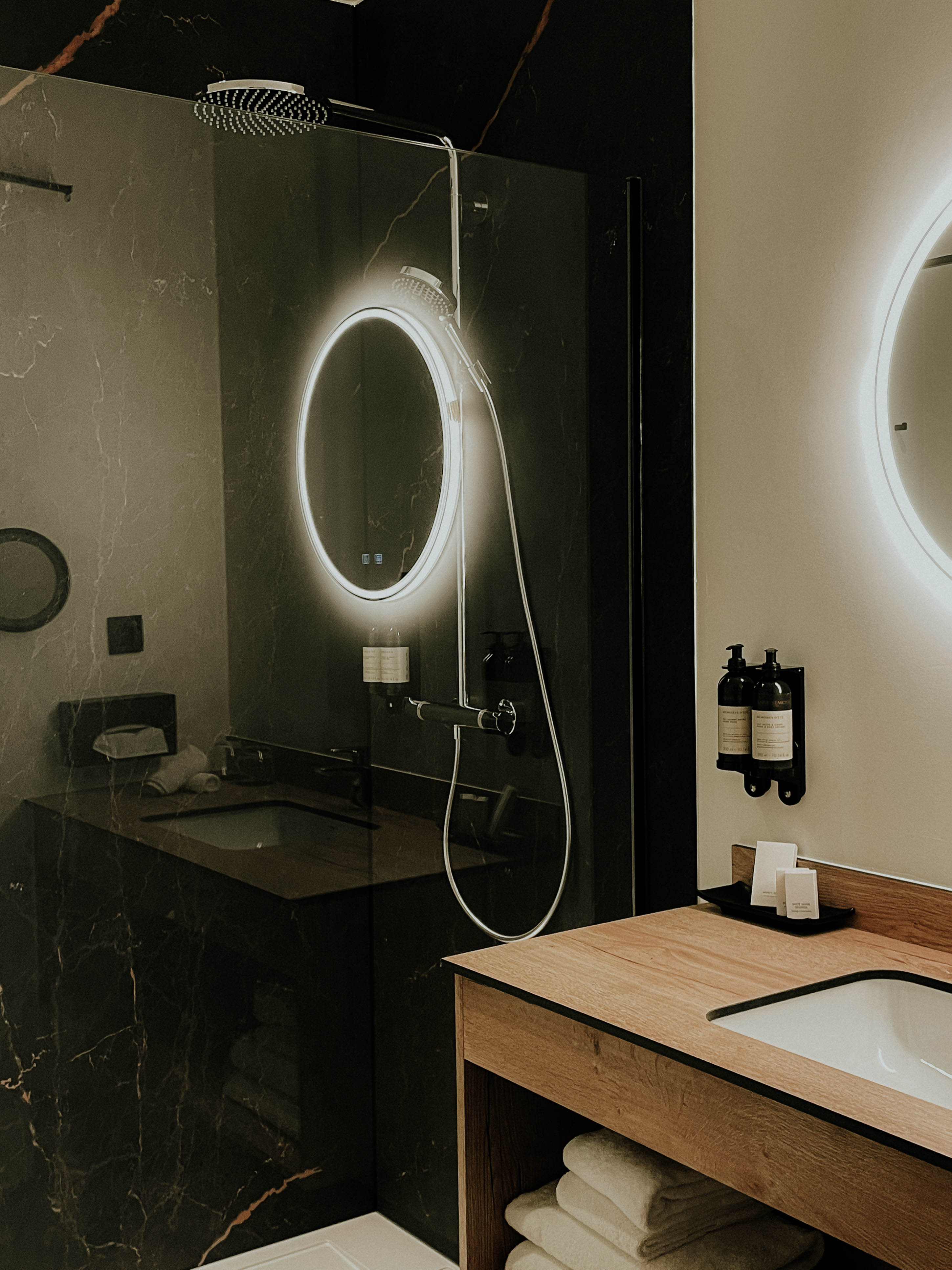 Badkamer met verlichte ovale spiegel en donkere marmeren tegels